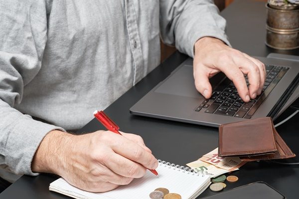 Close-up of a businessman or accountant holding pen working at desk using a laptop to calculate financial report or tax payments. Business concept of accounting, paying taxes, calculating finances