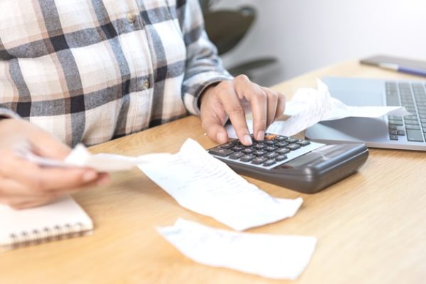 Business woman pressing the calculator calculate the various costs that must be paid by the bill invoices held and placed on the table.